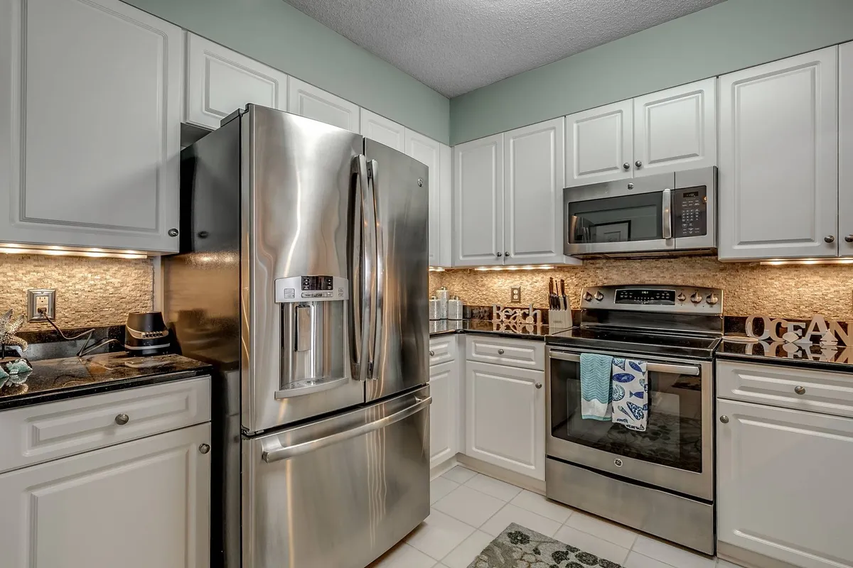 A modern kitchen with stainless steel appliances, granite countertops, and coastal-inspired decor. The layout is suited for group meal preparation and casual entertaining, with ample space for cooking and conversation.