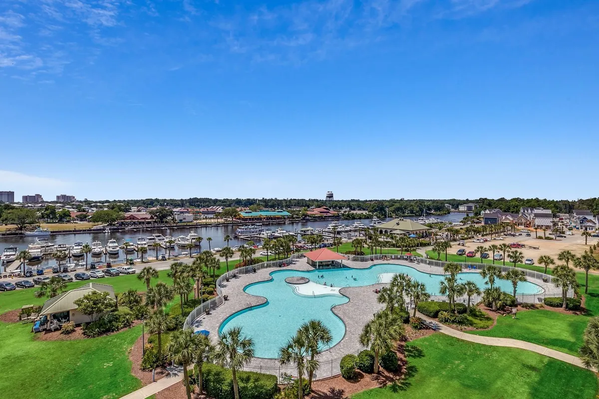 A vibrant exterior scene featuring the resort’s expansive saltwater swimming pool, with a marina full of boats just beyond, lush green lawns, and inviting pavilions. The area is bustling with guests enjoying swimming, boating, picnicking, and socializing, embodying the active and resort-like atmosphere described in the section.